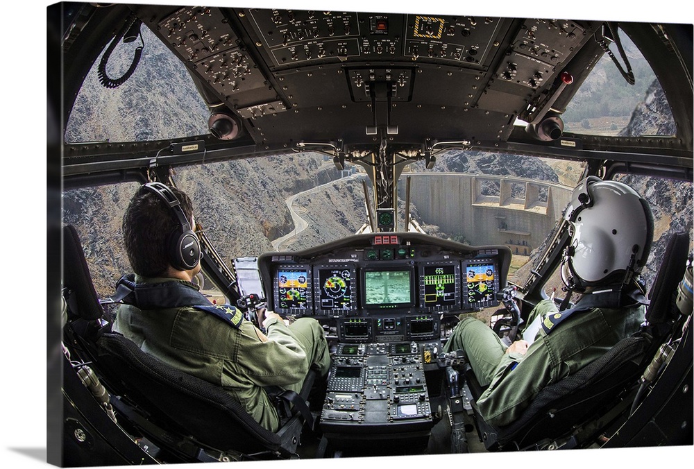 Two pilots sitting in the cockpit of an airplane looking at a dam out the window.