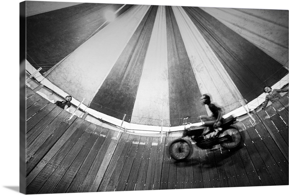 Motorcyclist riding on the wooden walls of a circus tent in a daredevil act.