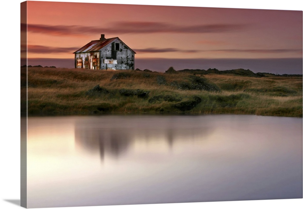 An abandoned farm house on the grassy shore by a lake in Iceland, at sunrise.