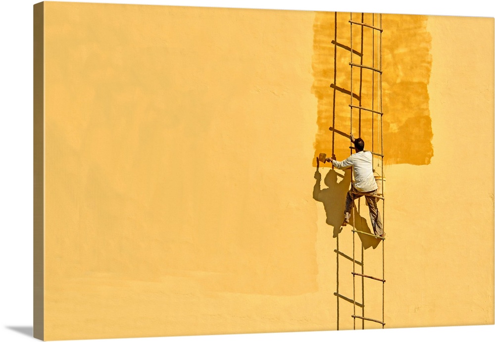 A man on a precarious ladder painting the side of a wall yellow, Jaipur, India.