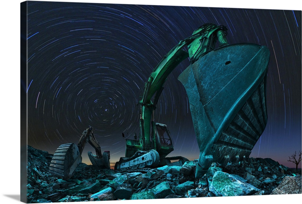 Wide angle photo of two excavators under the night sky with star trails.