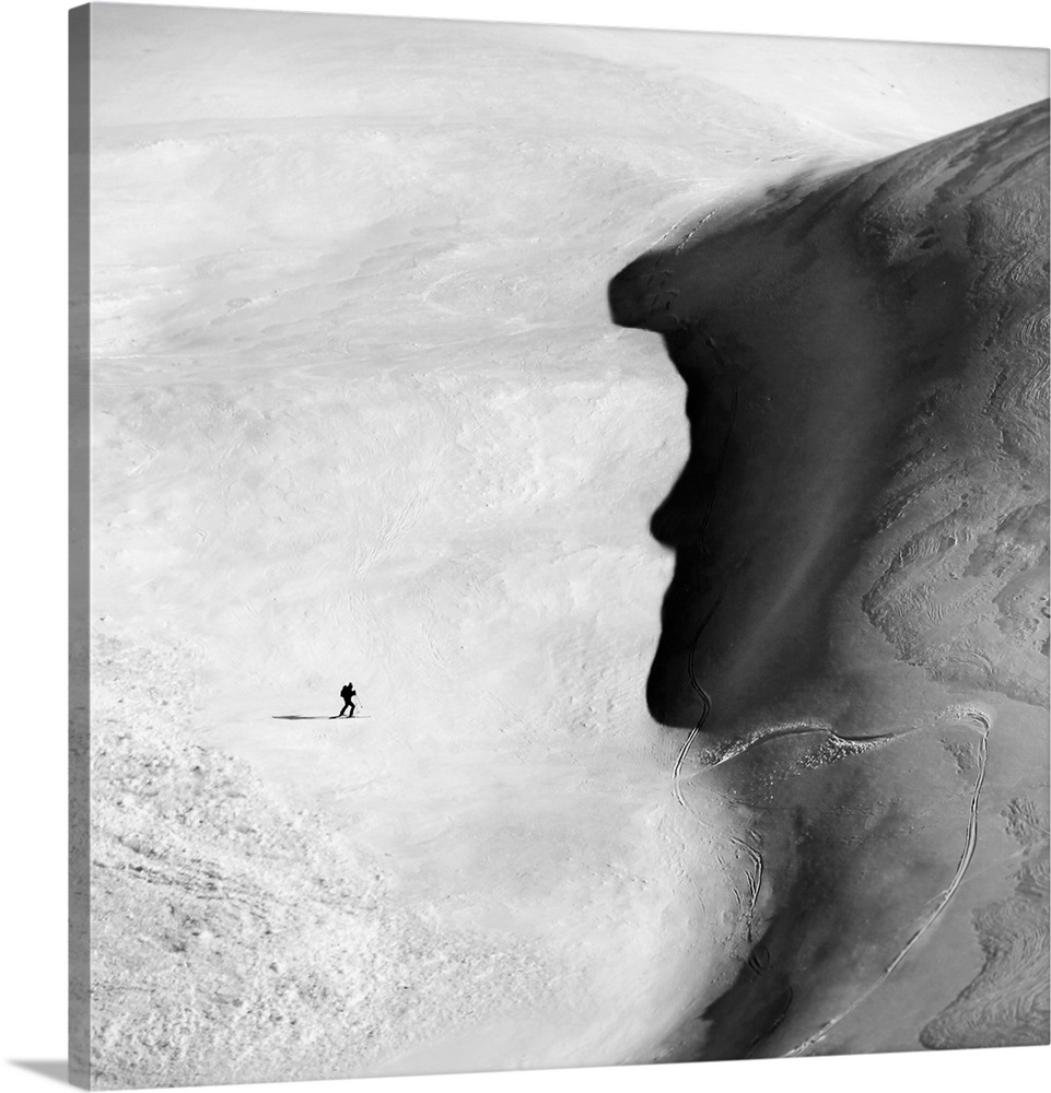 A skier trekking across a snowy plain towards a shoreline which resembles a face in profile.
