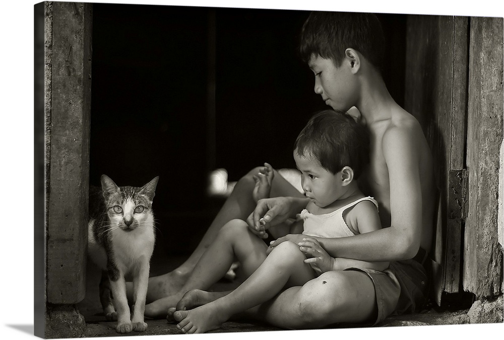 A boy holding his younger brother sitting in a doorway, looking at a small cat.