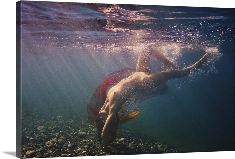 A nude woman dives in the water with a red veil, illuminated by beams of light shining through the surface.