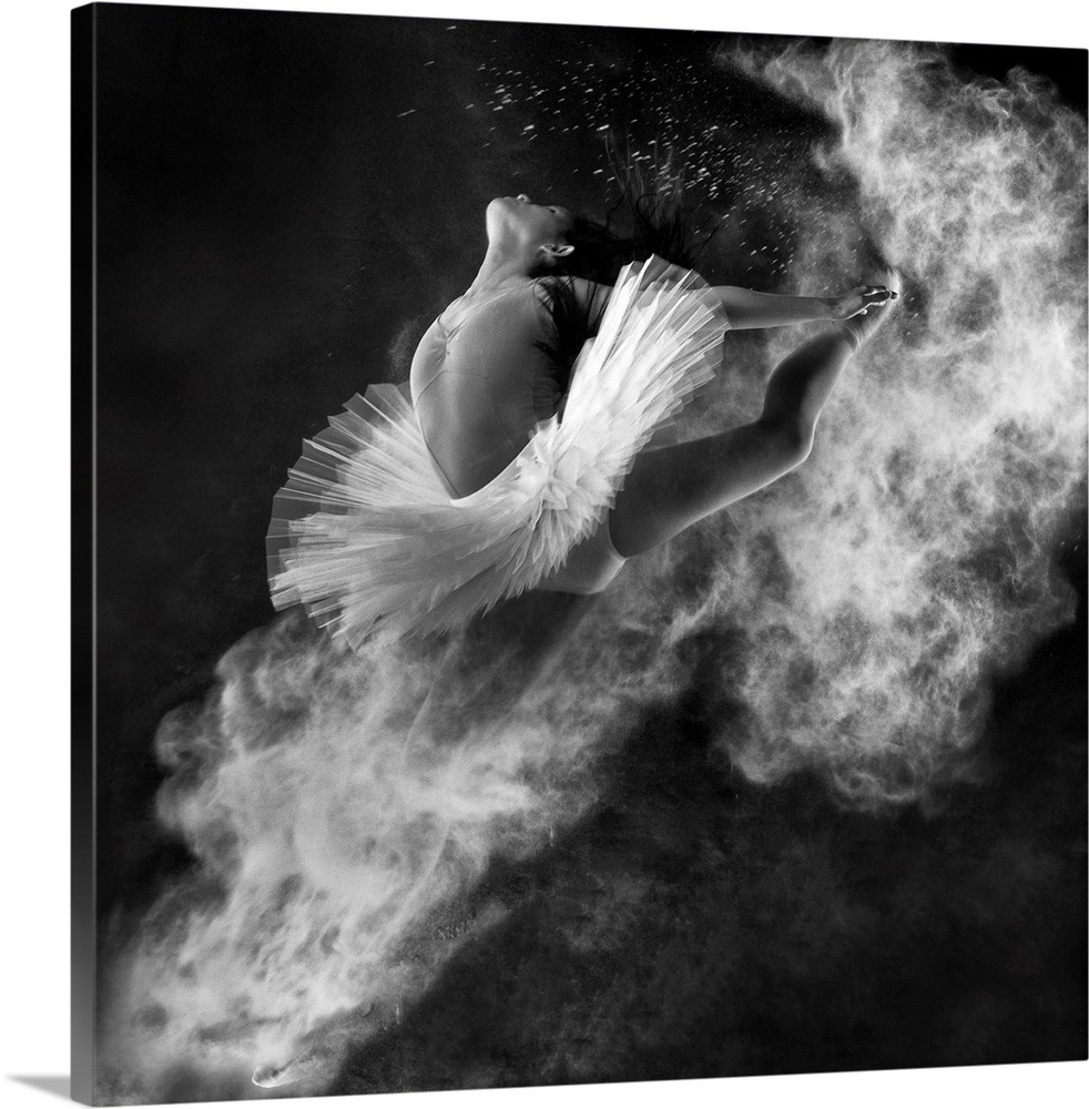 A black and white photograph of a dancer leaping into the air with dust kicking off her hands and feet.