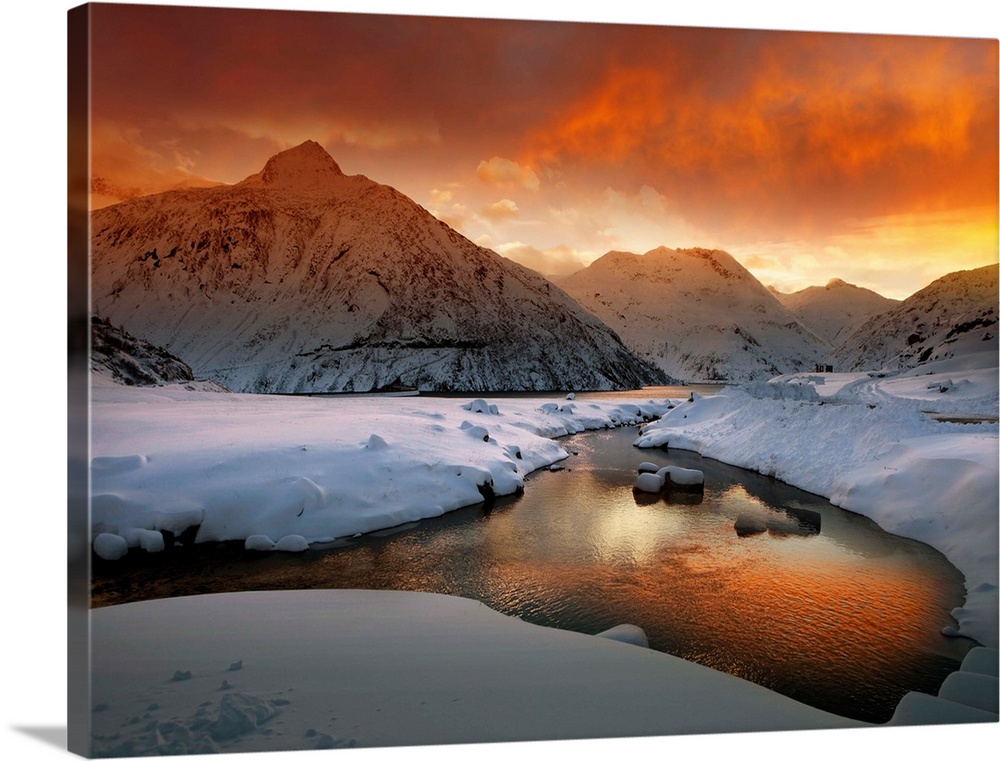 A river in a snowscape reflecting the orange color of the sunrise, in the Austrian Alps.