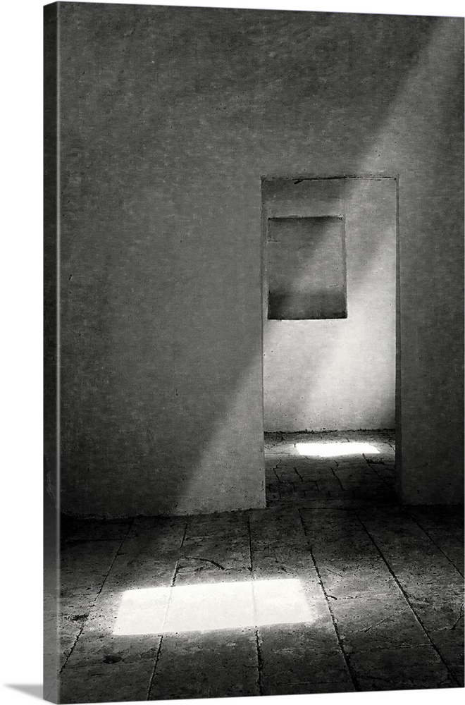 A ray of light shining into a bare room with a view through a doorway to another window.