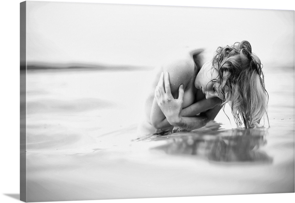 Black and white fine art portrait of a nude woman in freezing water, holding herself.