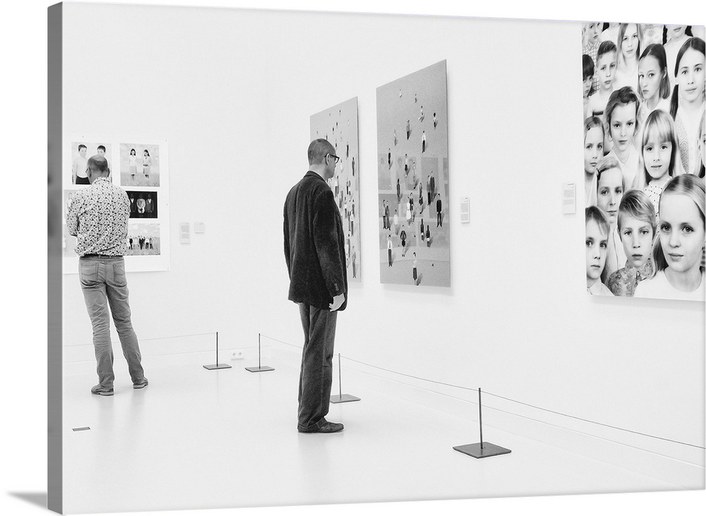 A man in an art gallery looks at figurative artwork on the wall.