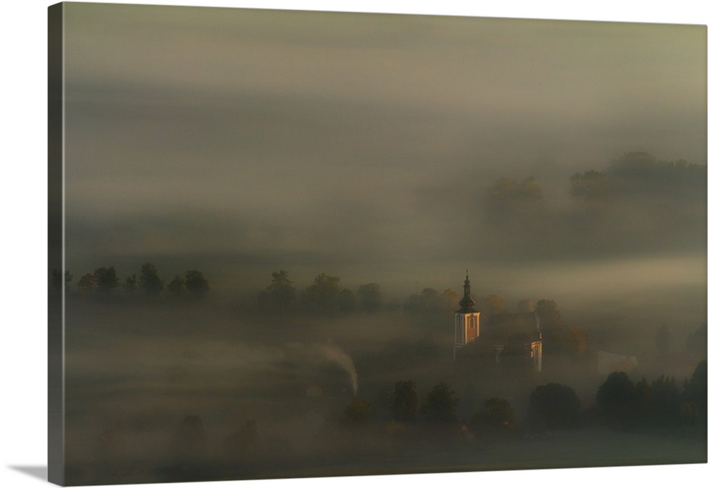 Church spire rising through the thick blanket of fog that covers this countryside scene.