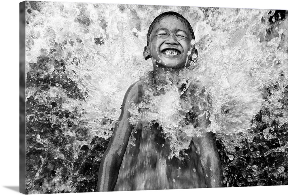 A young boy smiling as he's splashed by water from the river, Indonesia.