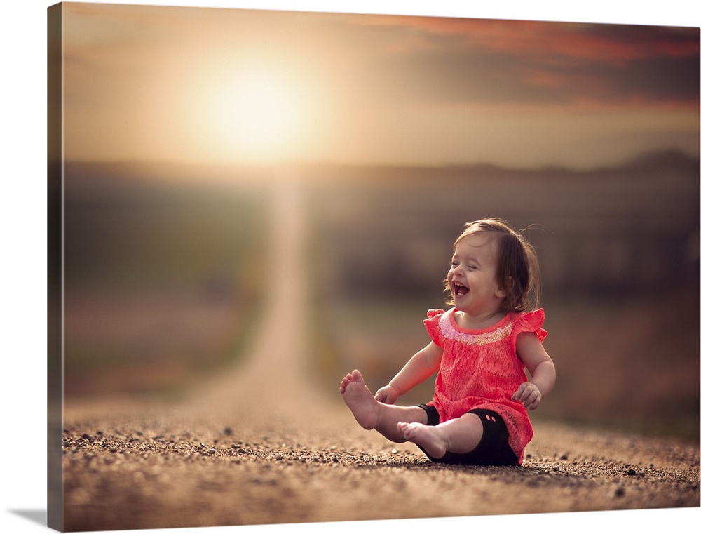 A happy baby girl laughing on a gravel path at sunset.