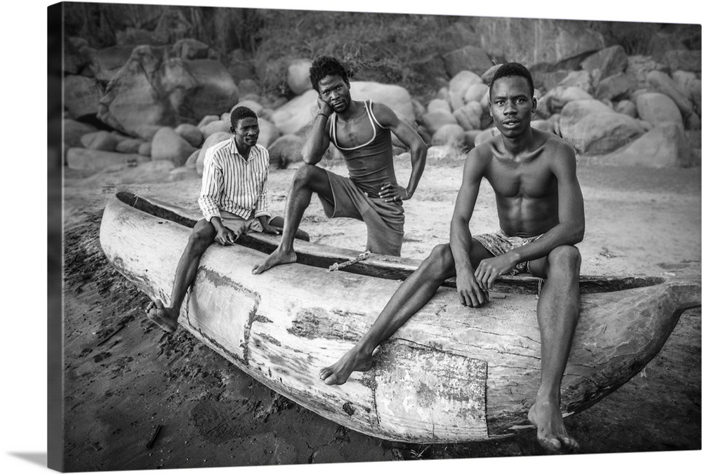 Three fishermen from Malawi posing with their canoe on the beach.