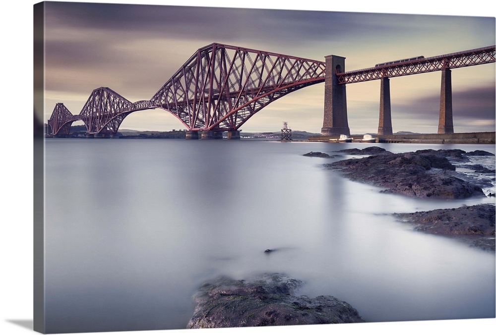 View from the rocky shore of the criss-crossing beams of a bridge in Edinburgh, Scotland.