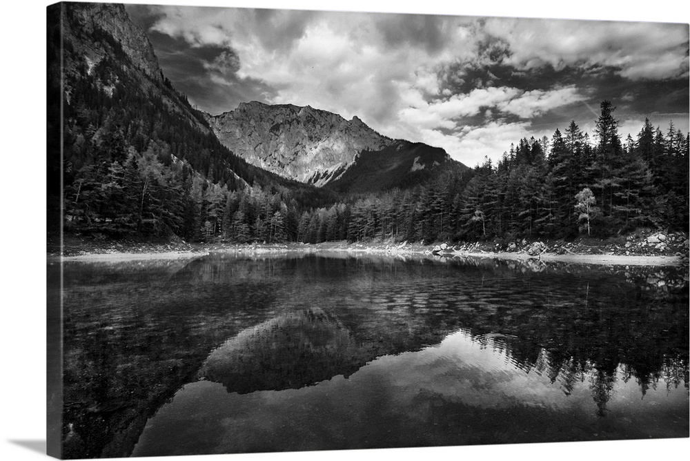 A black and white photograph of a wilderness scene with a mountain range and forest reflecting in the lake below.