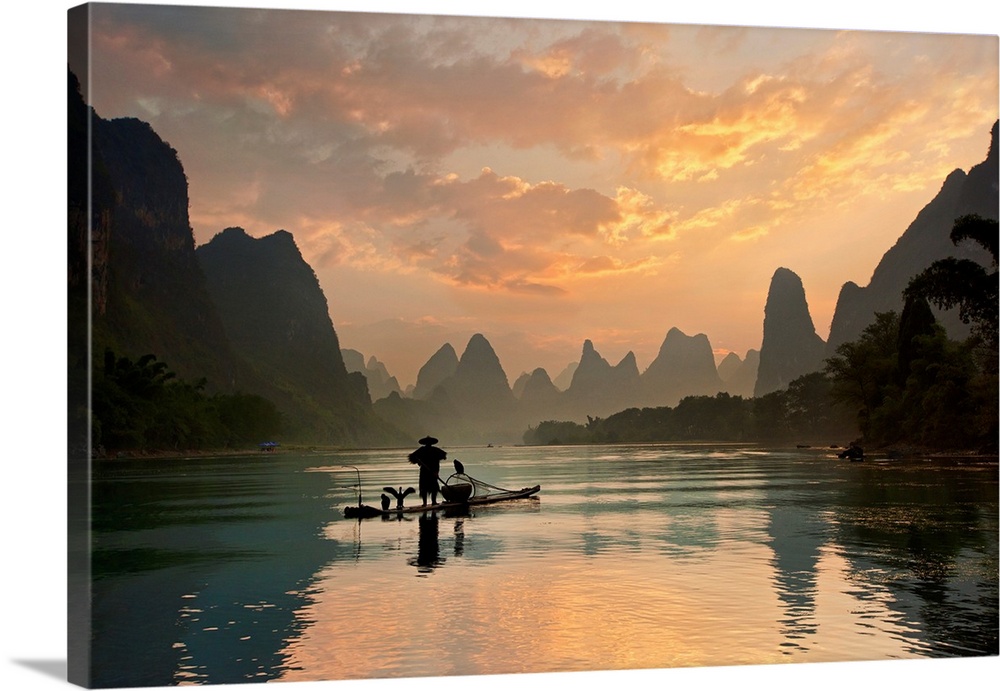 A fisherman and his cormorants on a boat in the Li River at dawn, China.