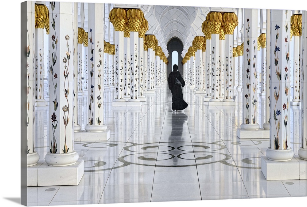 A woman in black robes walks down the archway of  the Sheikh Zayed Grand Mosque in Abu Dhabi, United Arab Emirates.