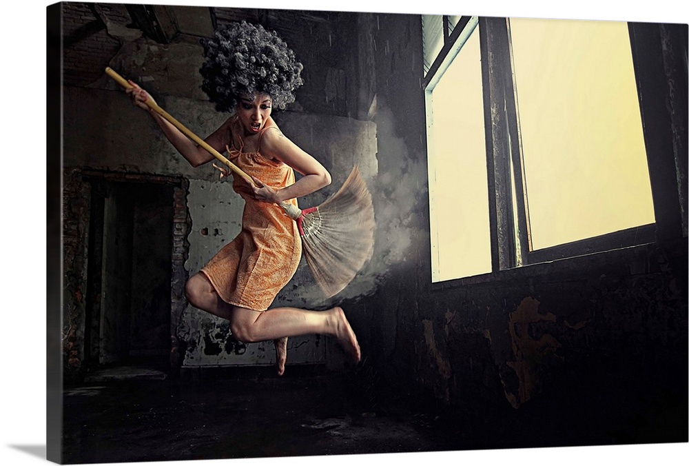 A women leaping into the air playing air guitar on a mop in front of a window.