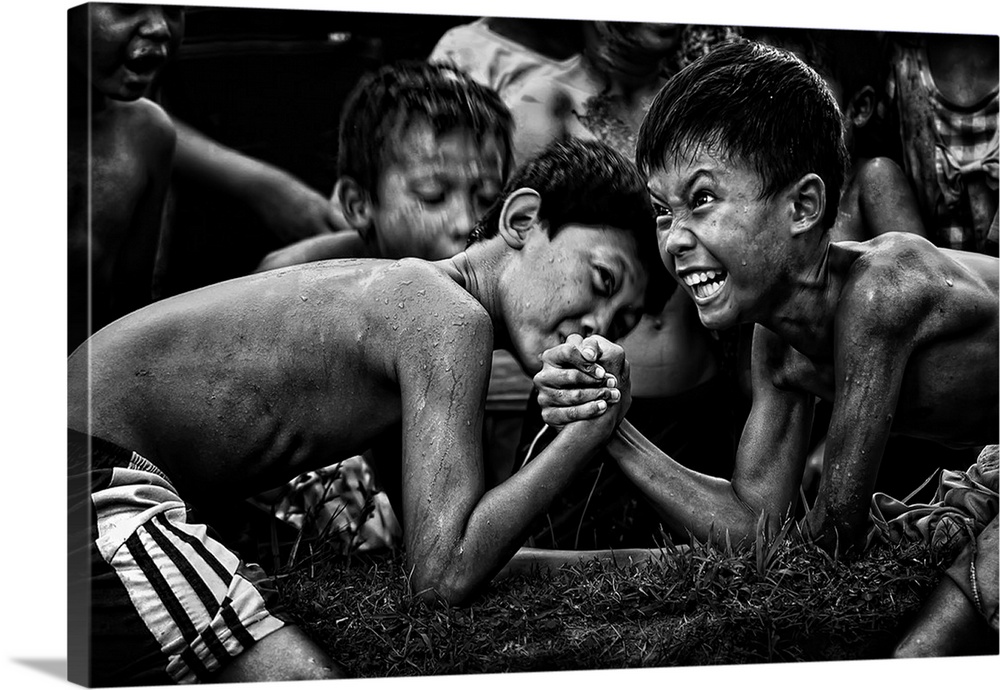 A black and white photograph of children arm wrestling with other gathered around them.