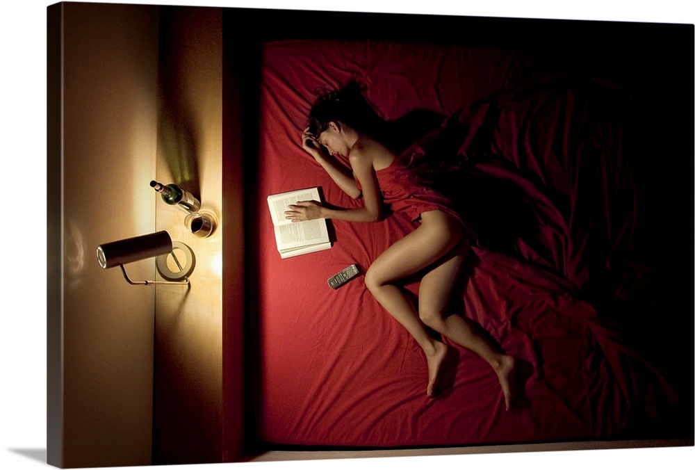 A woman wrapped in red sheets sleeping in a bed with a book and a bottle of wine.