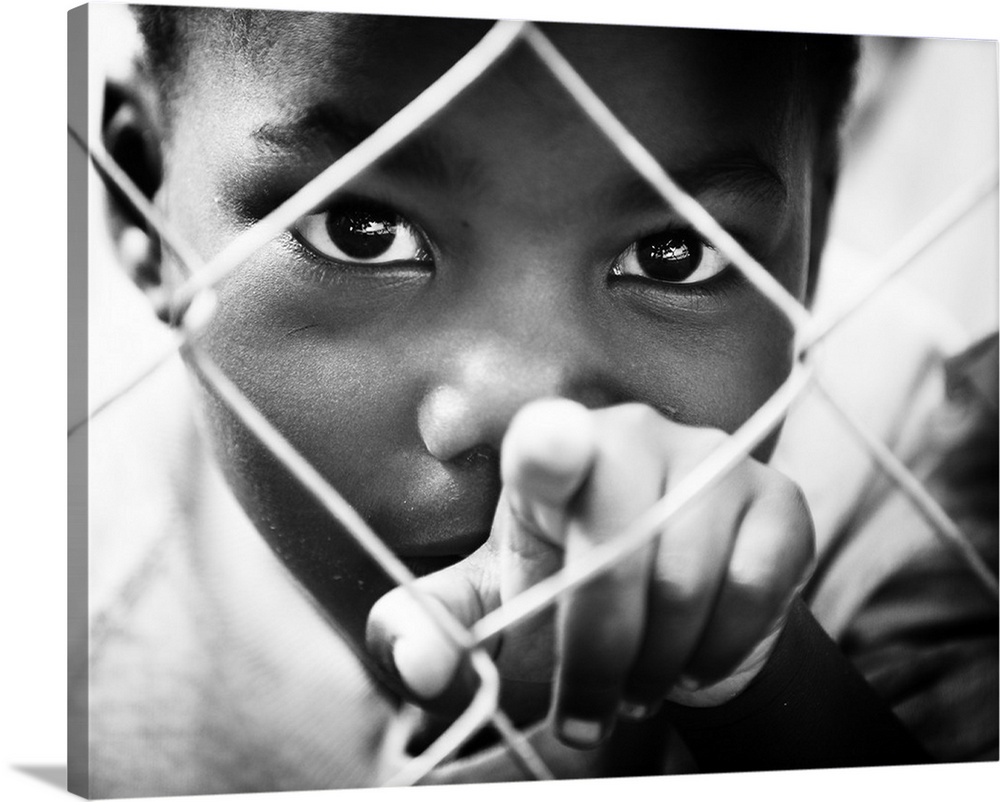 A small boy points through a chain-link fence.