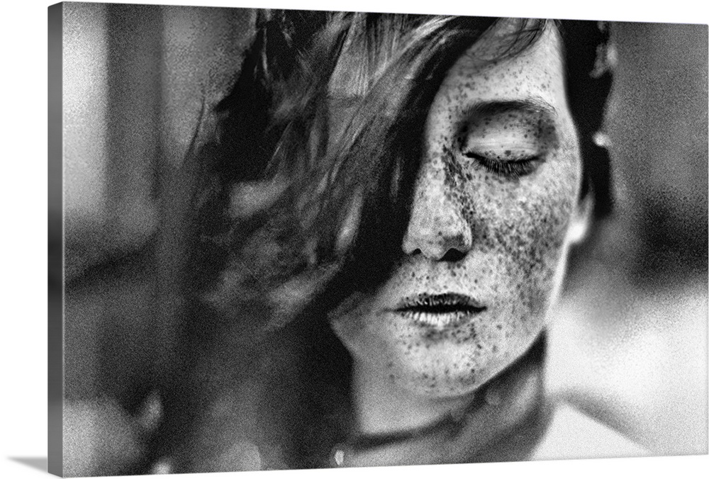 Black and white portrait of a young girl with freckles and hair covering one of her eyes.