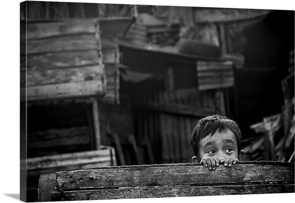 A small boy peeking his head out from behind a wooden fence in Padang, Indonesia.