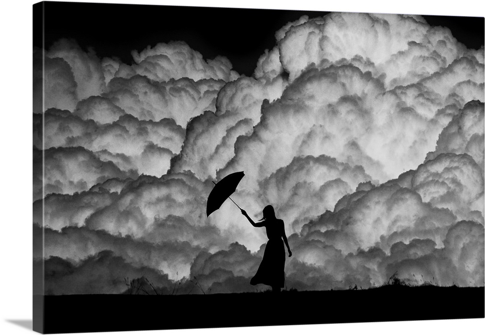 Silhouette of a woman with an umbrella in front of huge storm clouds.