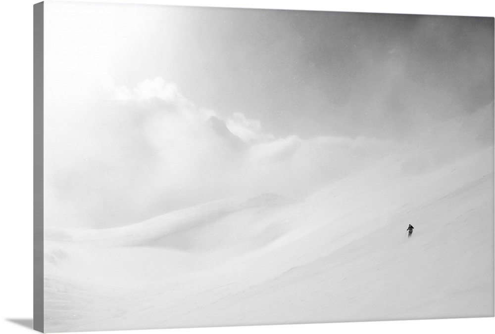 White mountain landscape of snow and clouds with a lone skier made miniature by the vast expanse.