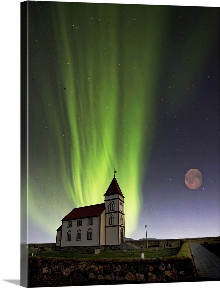 A church with a red roof and the lights of the aurora borealis glowing in the sky overhead, with a full moon.