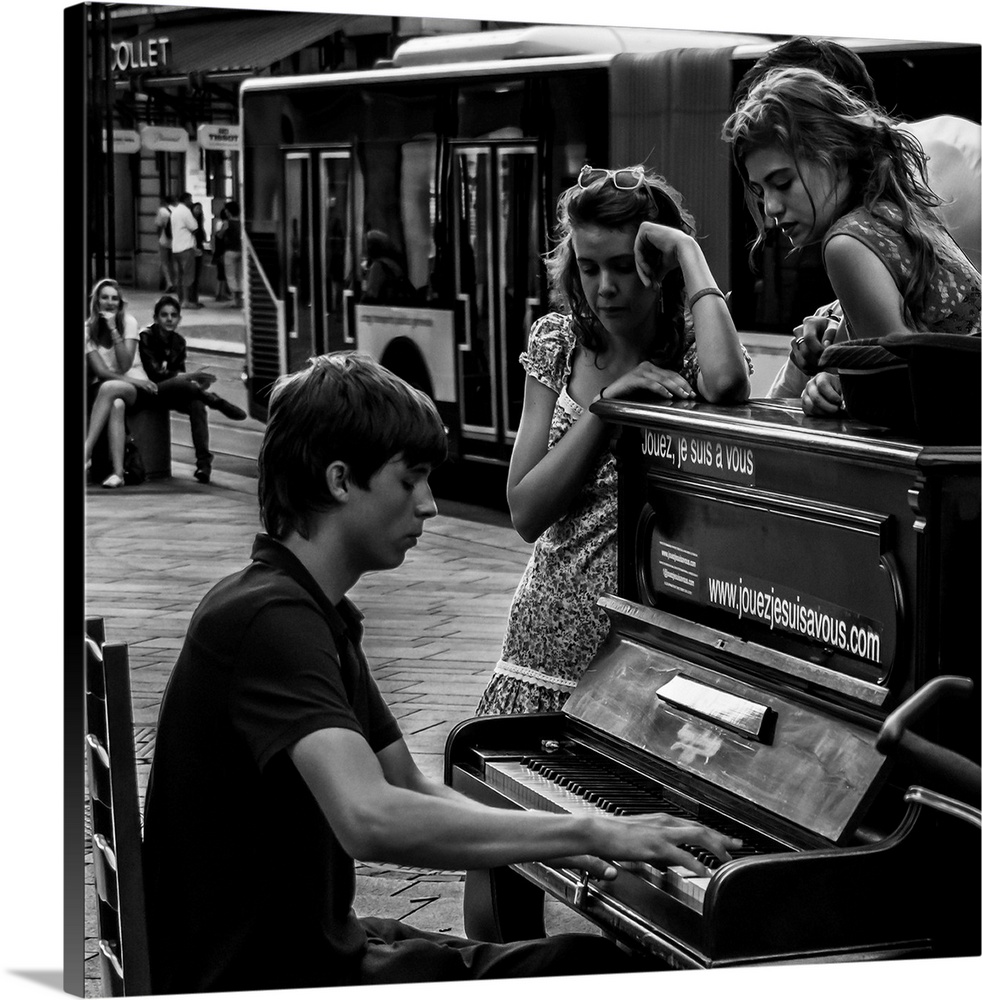 A black and white photograph of a man playing a piano in the street and women sitting around listening.