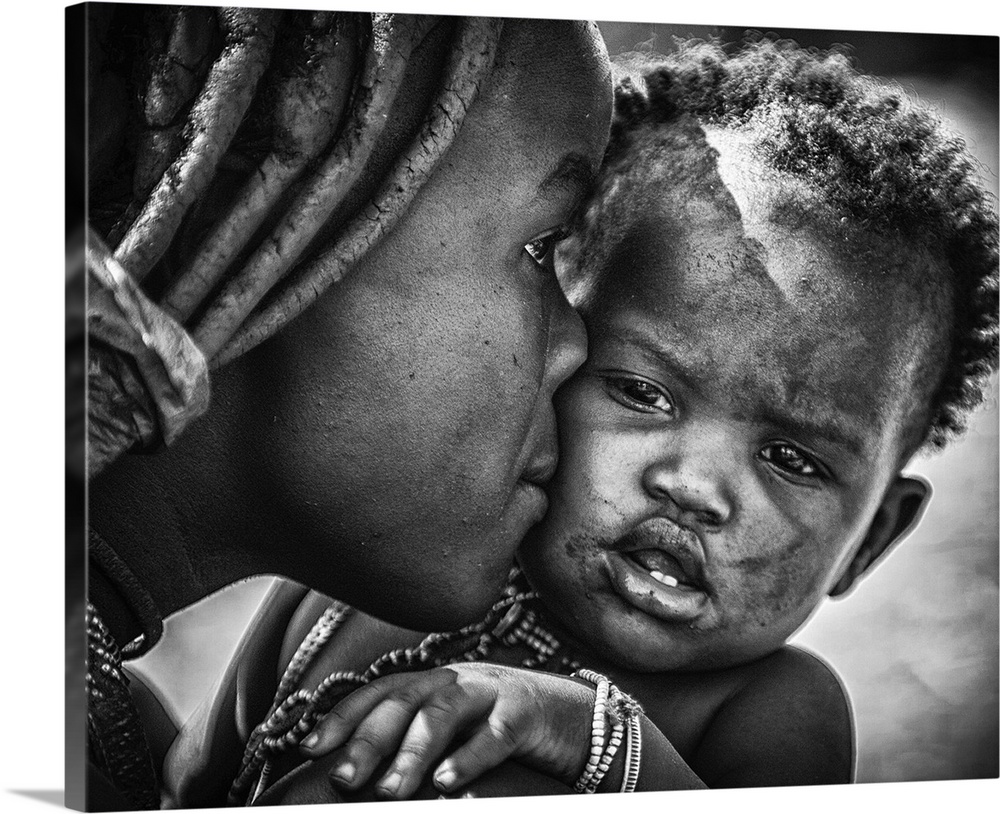 A young boy pulls a funny face as his mother kisses him, Namibia.