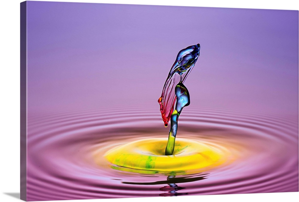 A macro photograph of a drop of water caught suspended in mid-air against a vibrant colorful background.