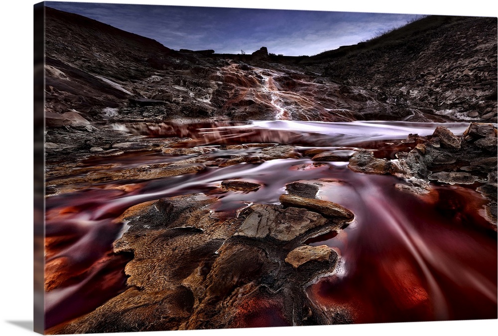 A red river flows through a rock landscape under a crescent moon, Spain.