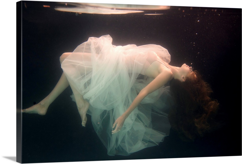 A conceptual photograph of a woman in white dress suspended under water.