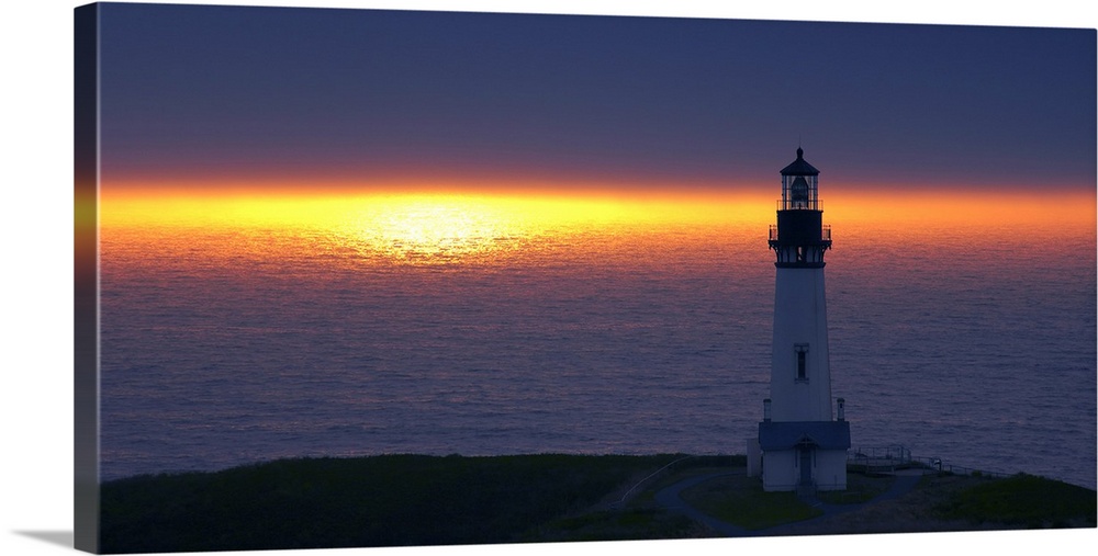 Landscape photograph of an unlit lighthouse at sunset by the ocean.