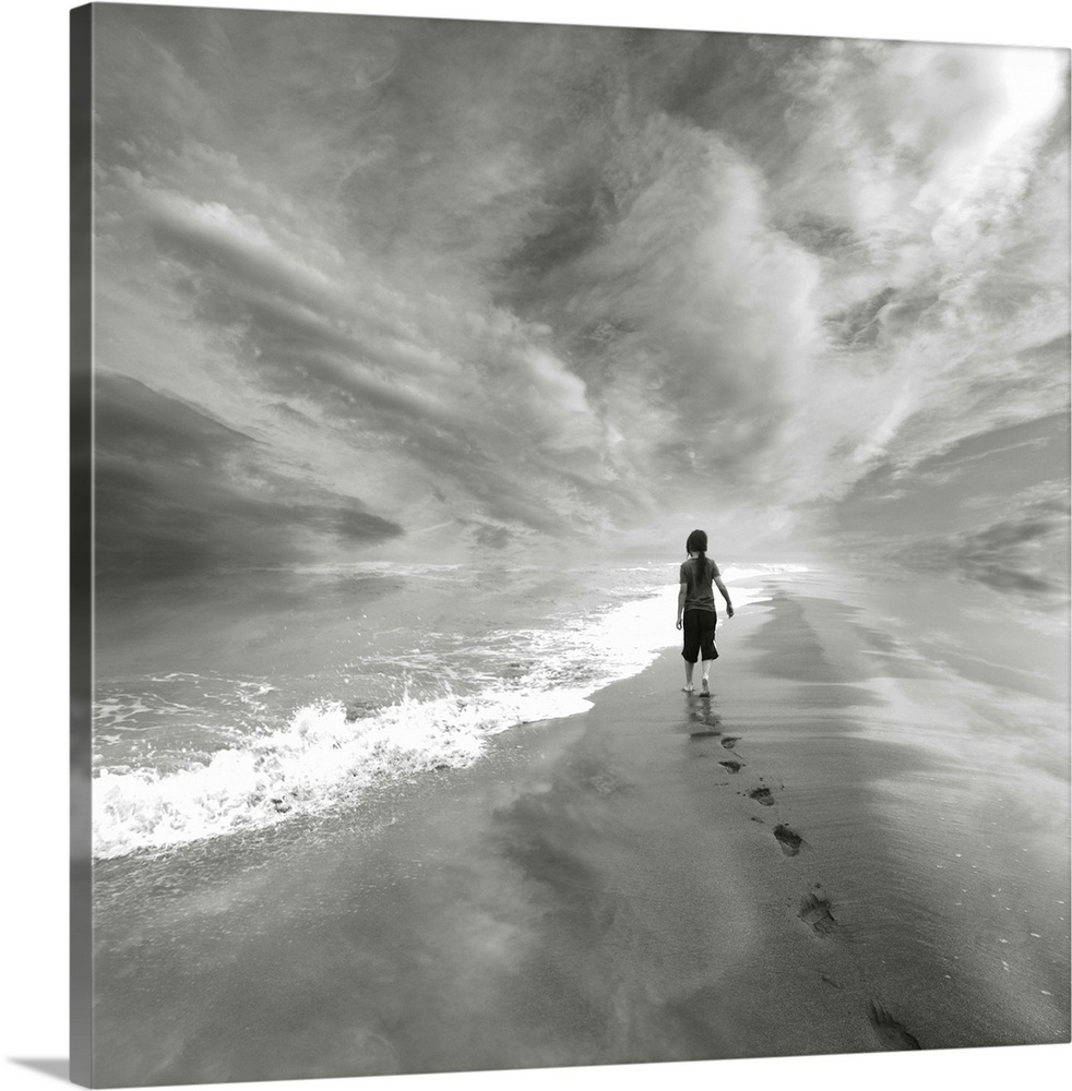 A young child walks along the beach to the edge of the water, leaving a trail of footprints behind.