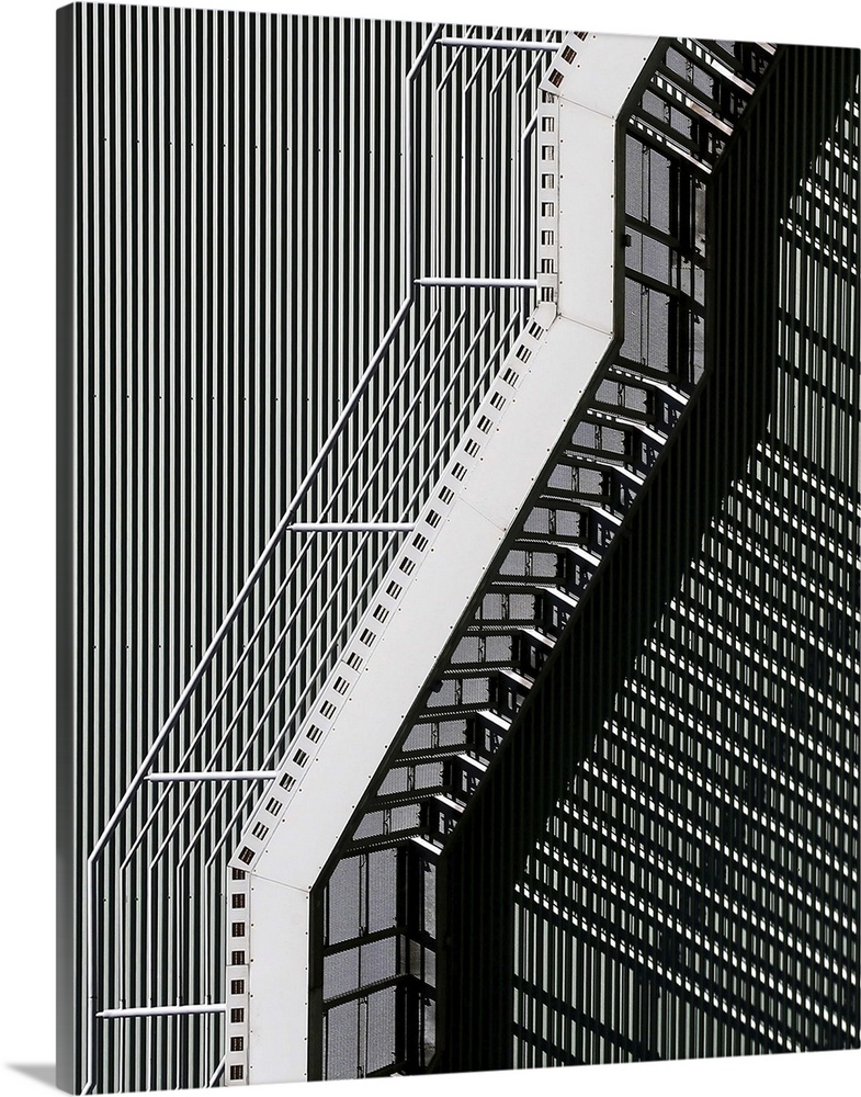 An outdoor metal staircase seen at n interesting angle, creates a complex pattern of shadows on the corrugated building.