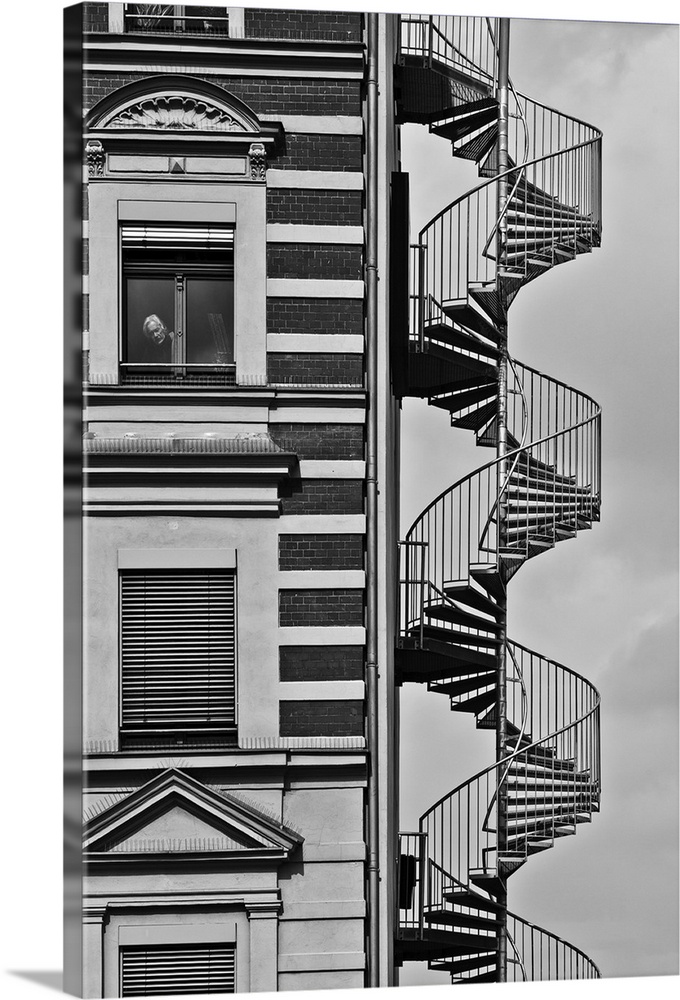 A spiral staircase against a building in Berlin, with a man looking out one of the windows.