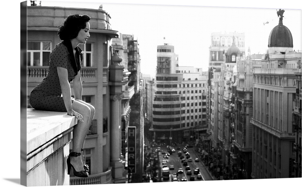 A woman sits on a ledge overlooking  the streets of Madrid.