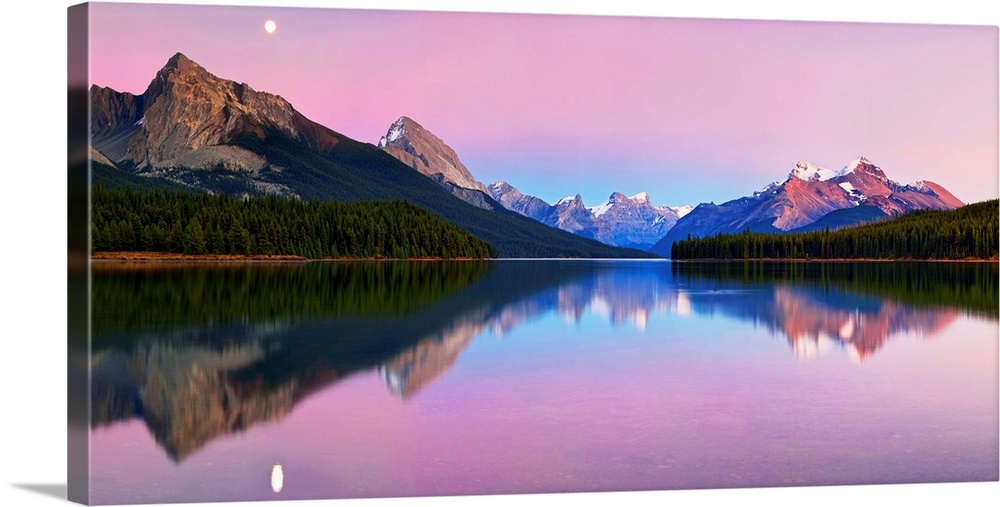 Panoramic image of calm Maligne Lake in the Canadian Rockies at twilight, with a mirror reflection of the mountains.