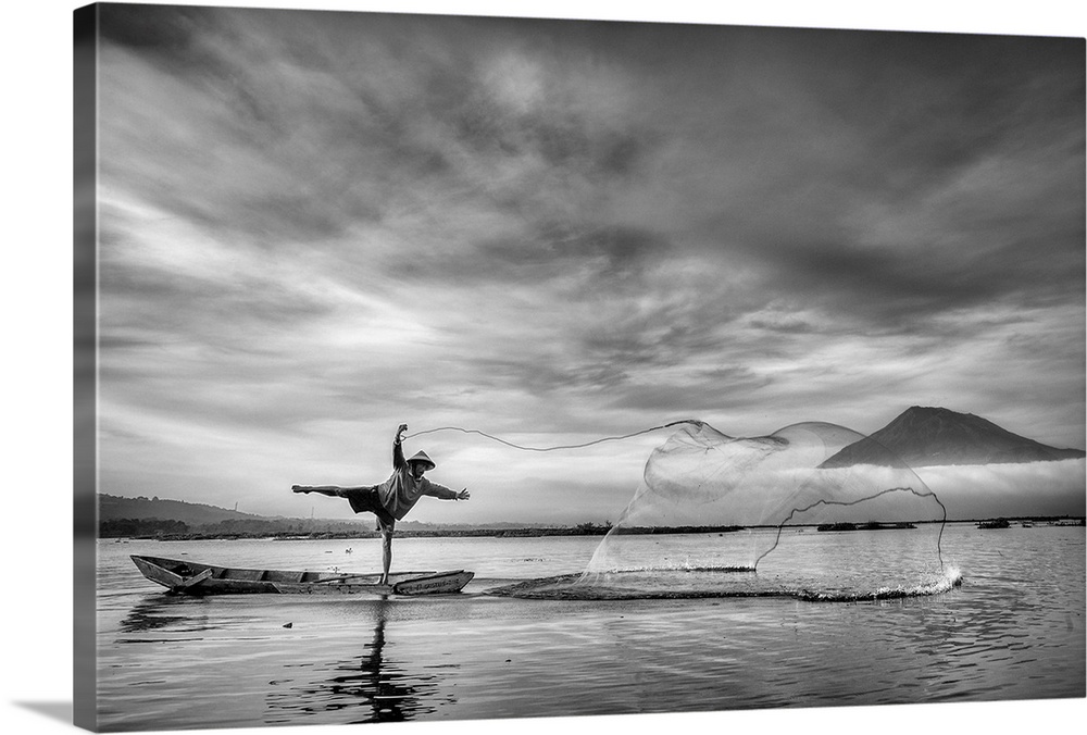 A man on a canoe strikes a pose as he skillfully throws a net into the water.