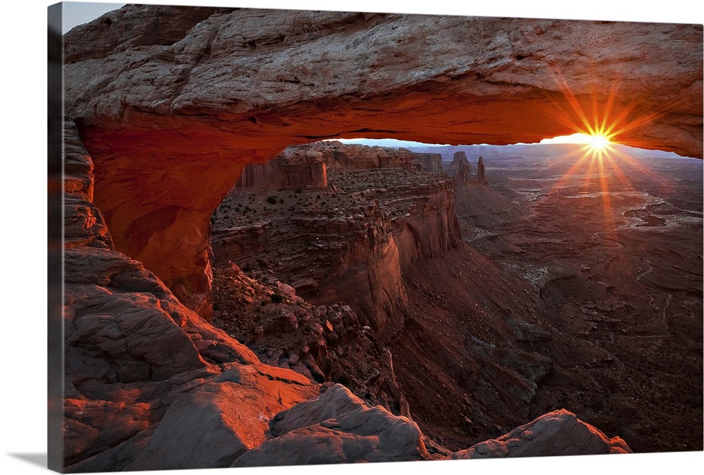 The sun framed by a large natural arch and the horizon, Canyonlands National Park, Utah.