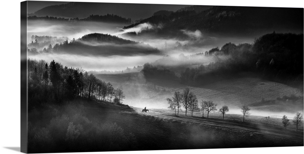 Black and white landscape with fog in the valley and a person riding a horse in the foreground.