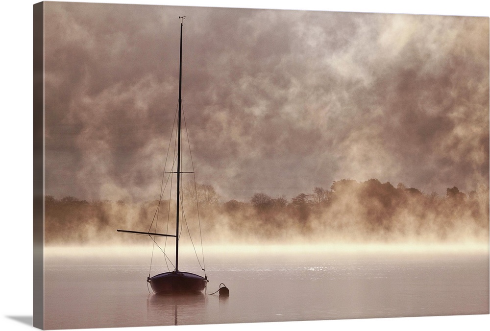 A boat with a tall mast in a misty lake in Cumbria.