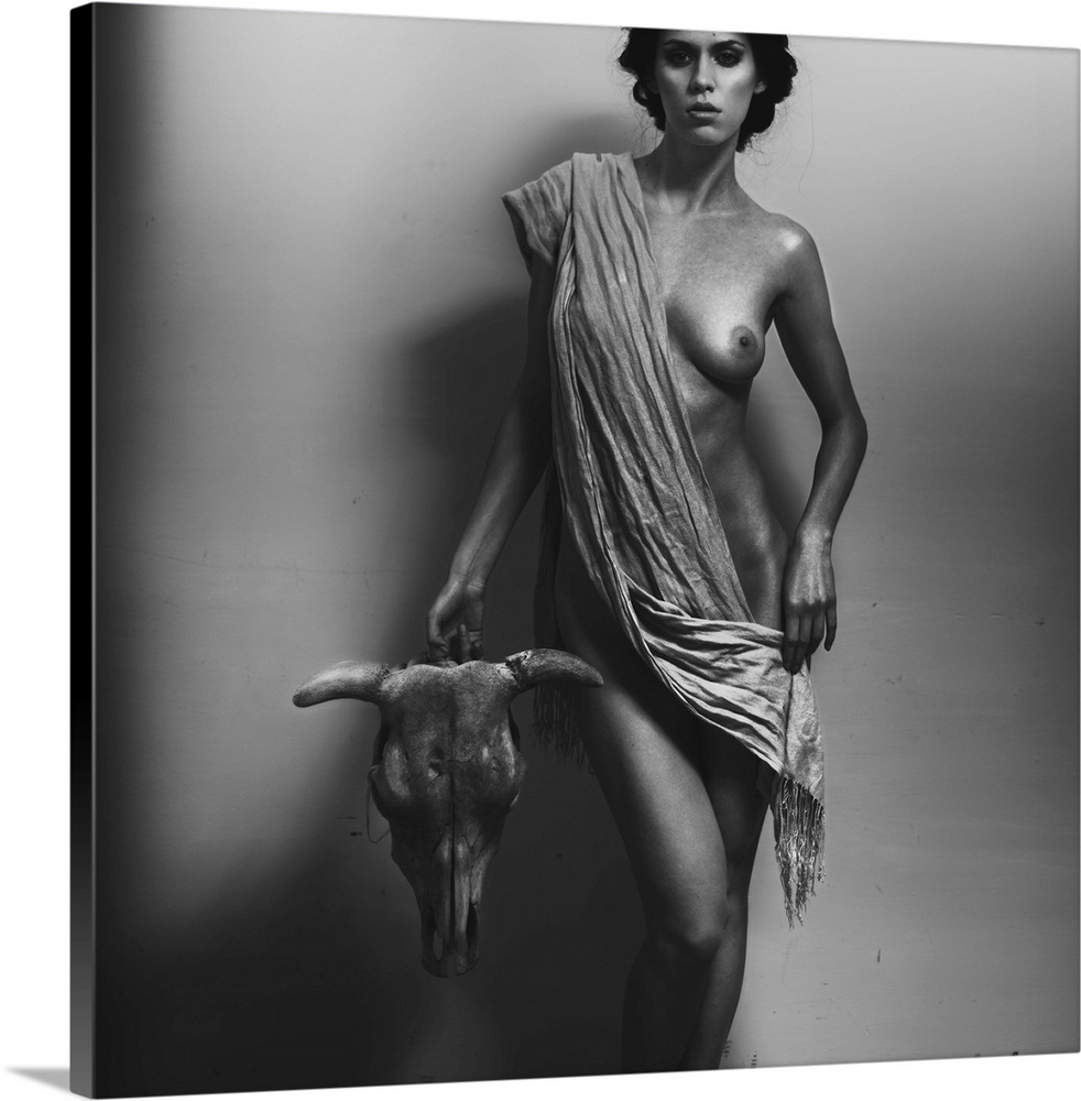 A black and white portrait of a nude woman draped in a cloth holding a bull skull.