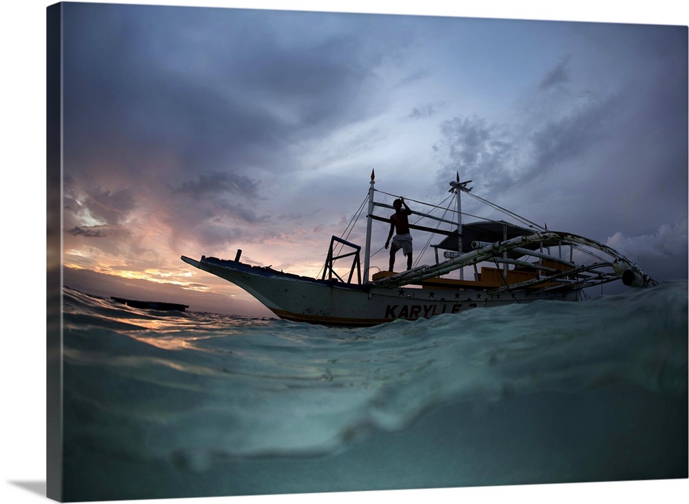 View from the surface of the water of a figure on a boat at sunset, Philippines.