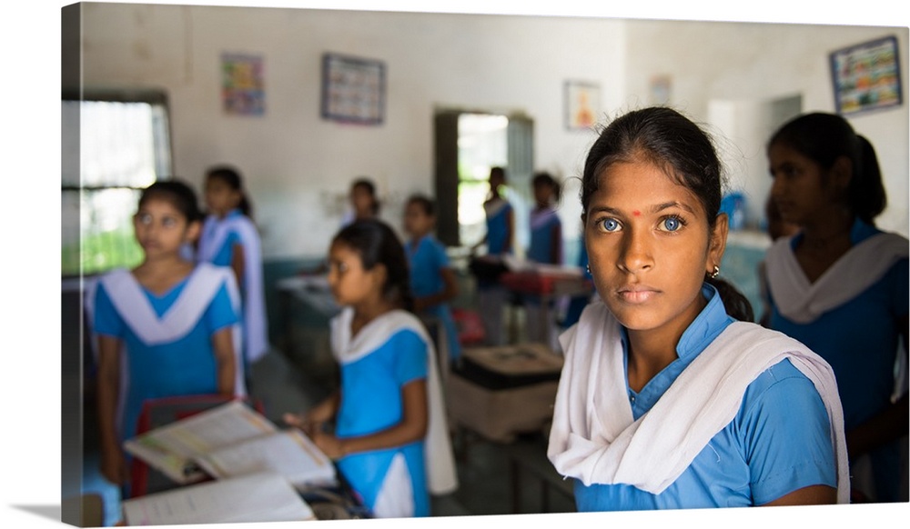 A young Indian woman with deep blue eyes in a classroom.