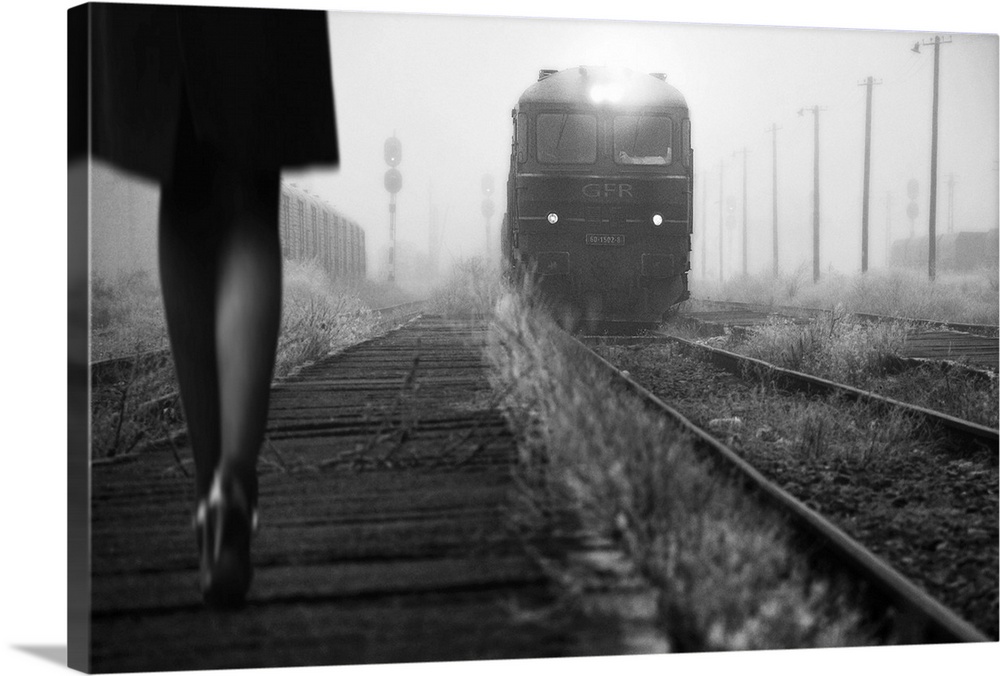 Black and white image of a woman in heels talking along a path by railroad tracks with an approaching train.