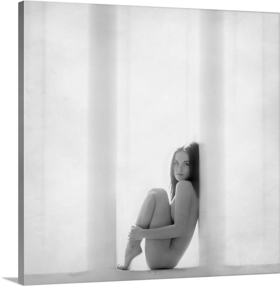 Nude woman curled up in a window frame in black and white.